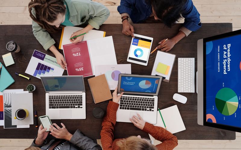 A small team seen from above, working through printed charts and laptops around a wooden table