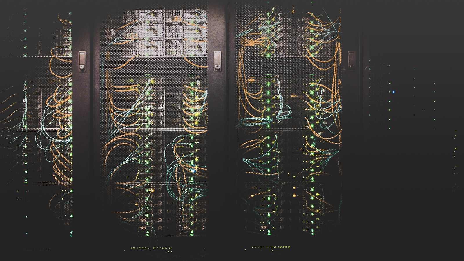 Server racks in a dark data center, patched with amber and teal network cables
