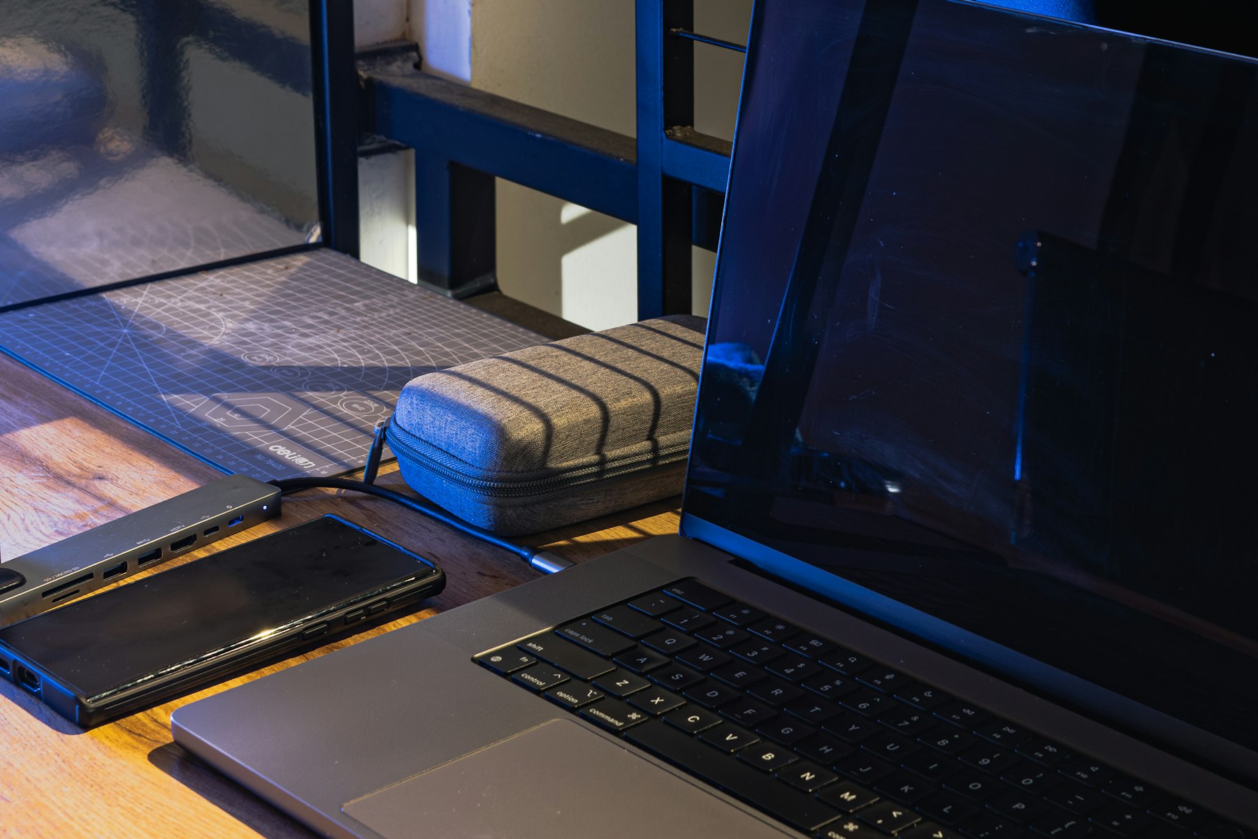 A laptop, a phone and a charger on a wooden desk in low light