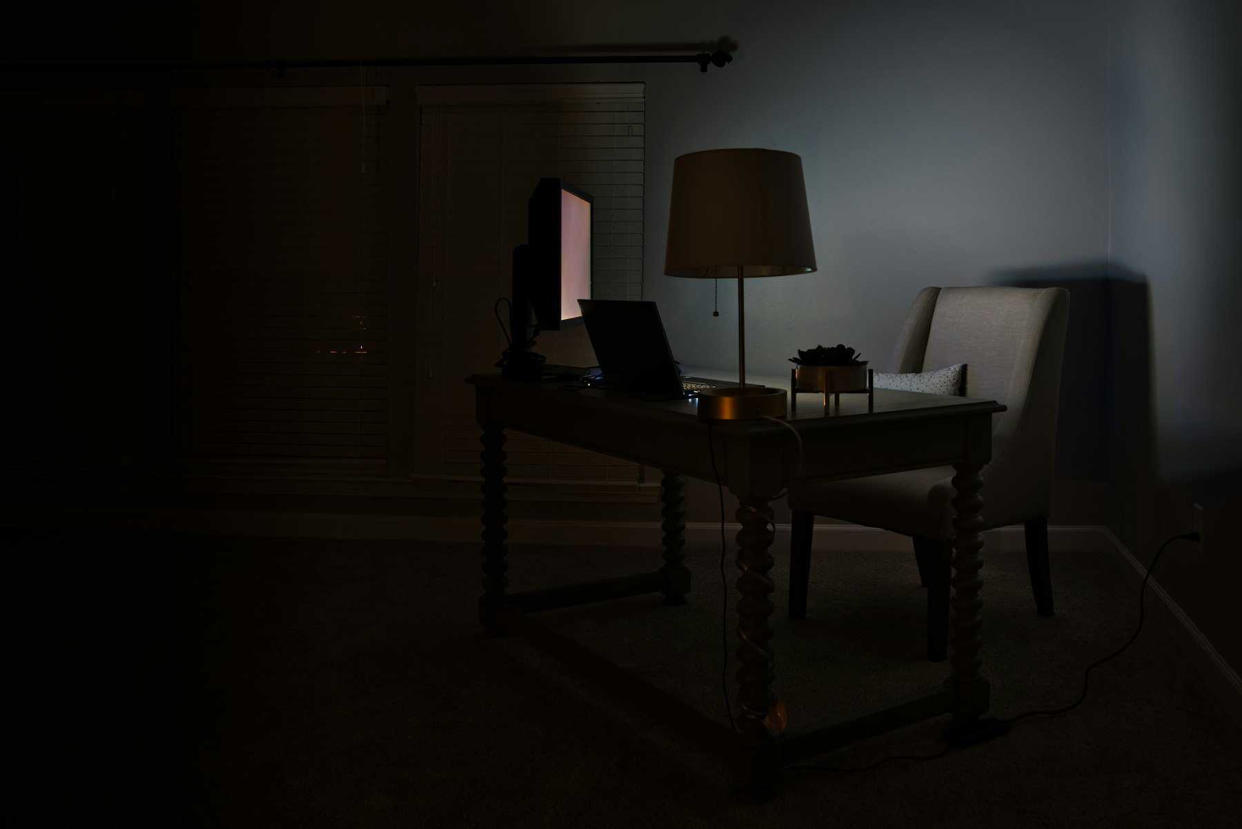 A desk with a monitor and a lamp in a dim room