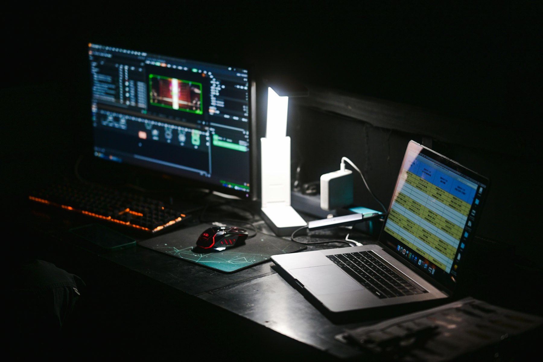 A monitor and a laptop on a dark desk, both screens lit