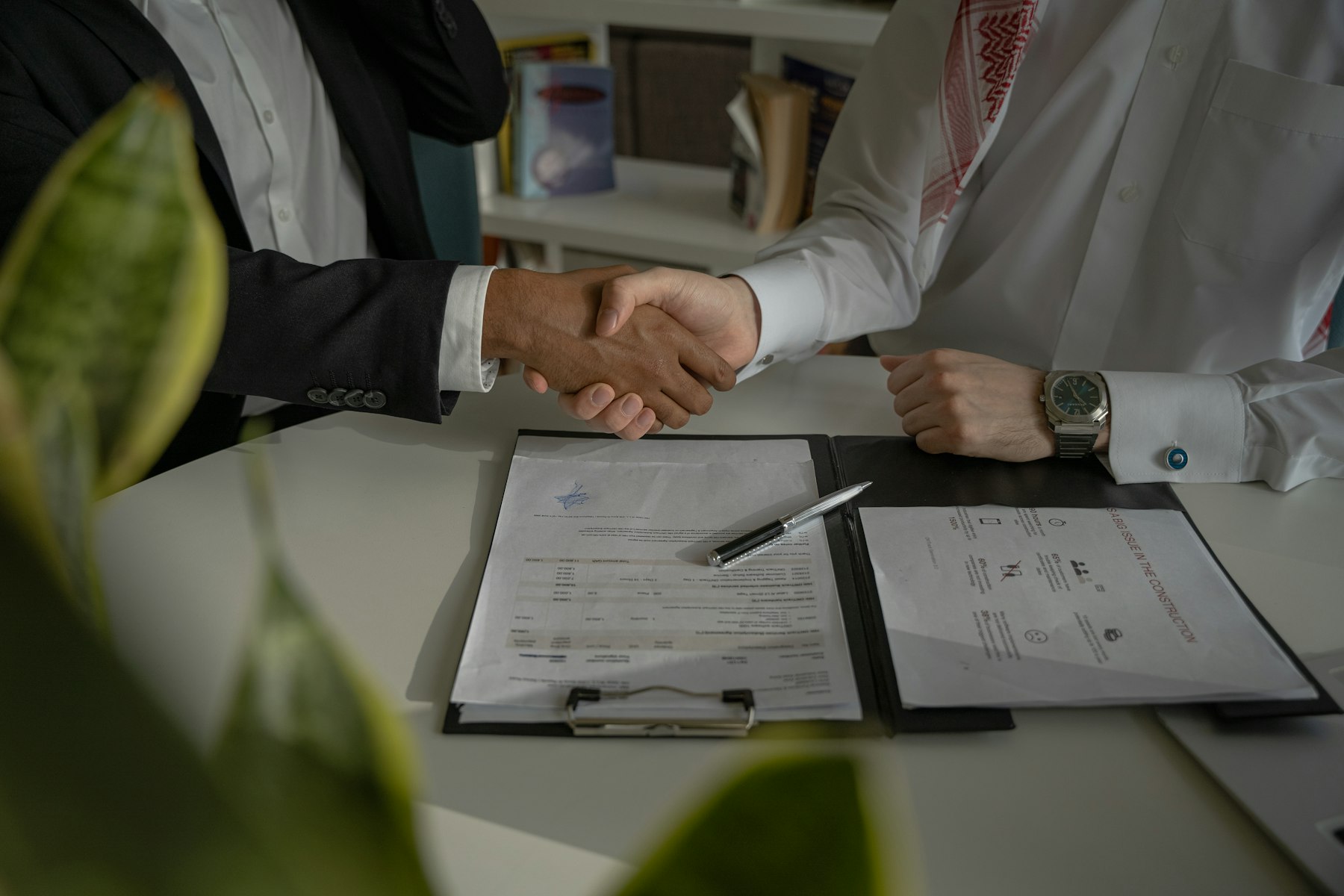 Two people shaking hands over a signed contract on a desk