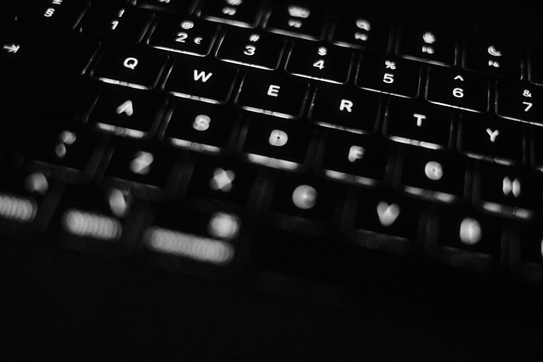 A backlit laptop keyboard glowing in a dark room