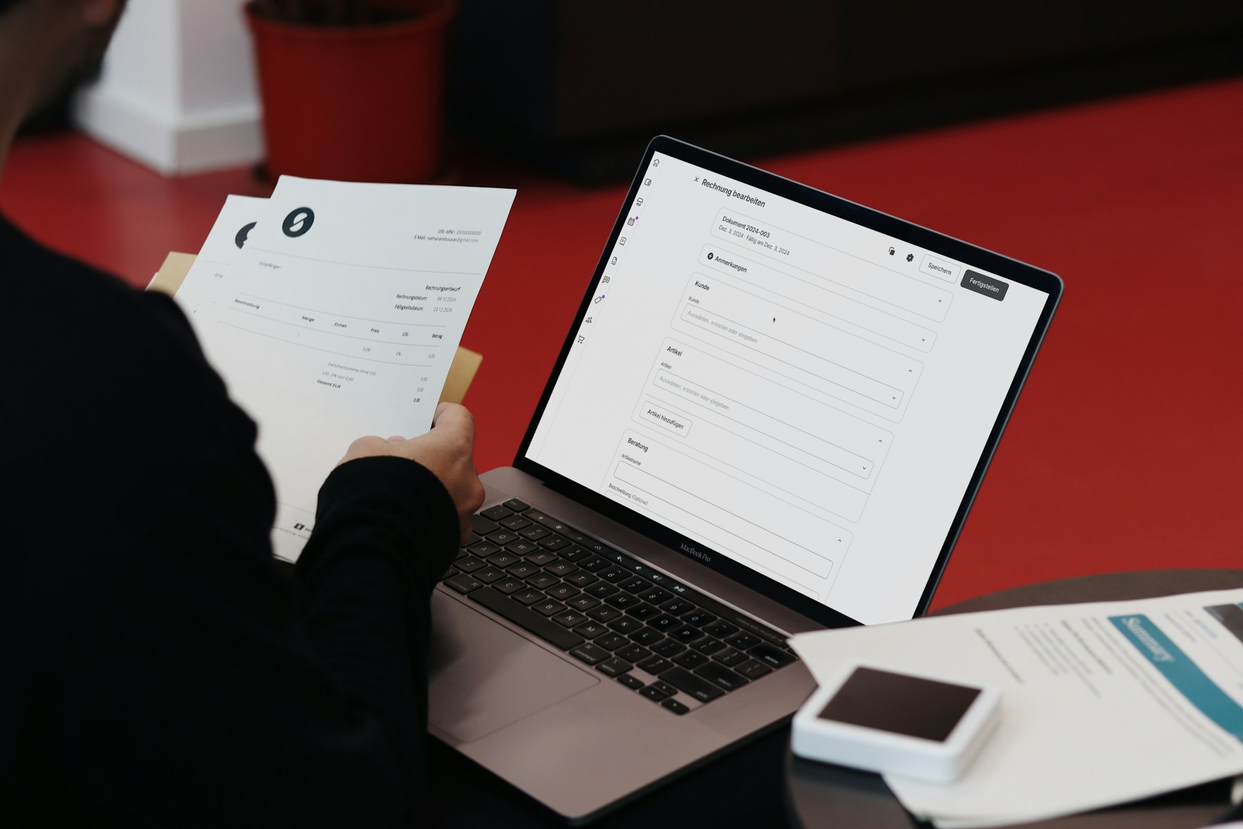 Hands sorting paper receipts beside a laptop showing an invoice form