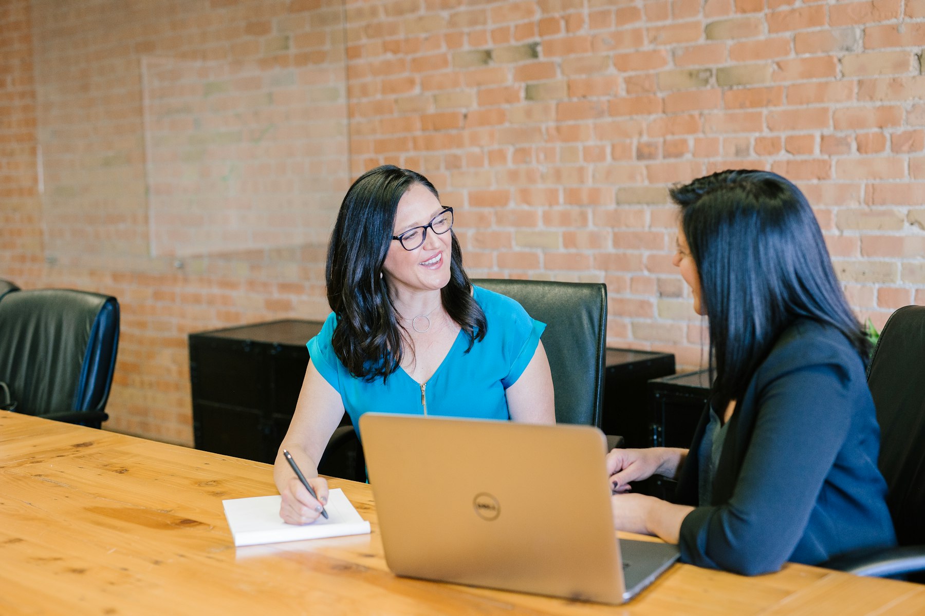 An advisor taking notes across the table from a client in a brick-walled office