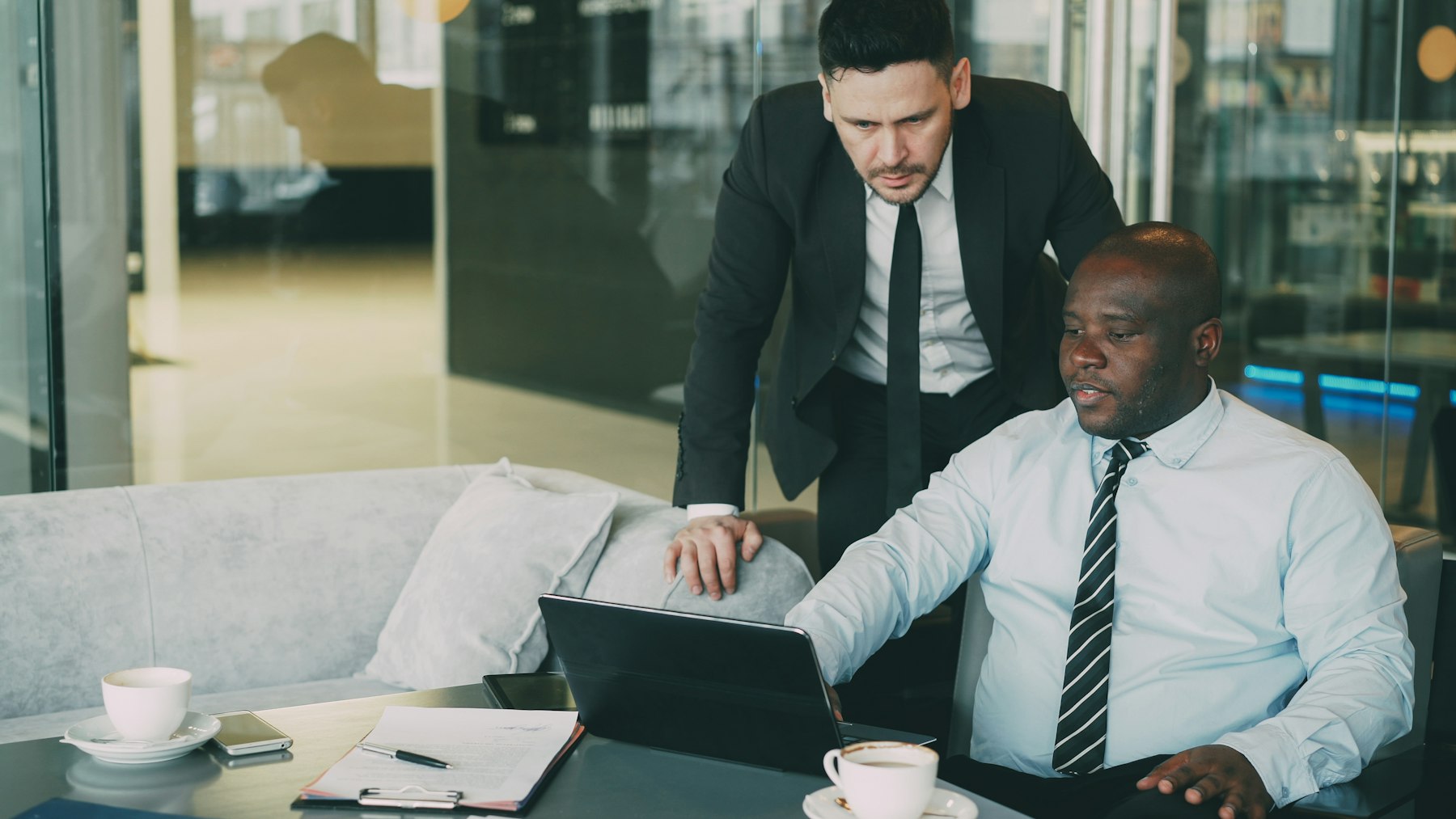 Two men going over something on a laptop in a glass-walled office