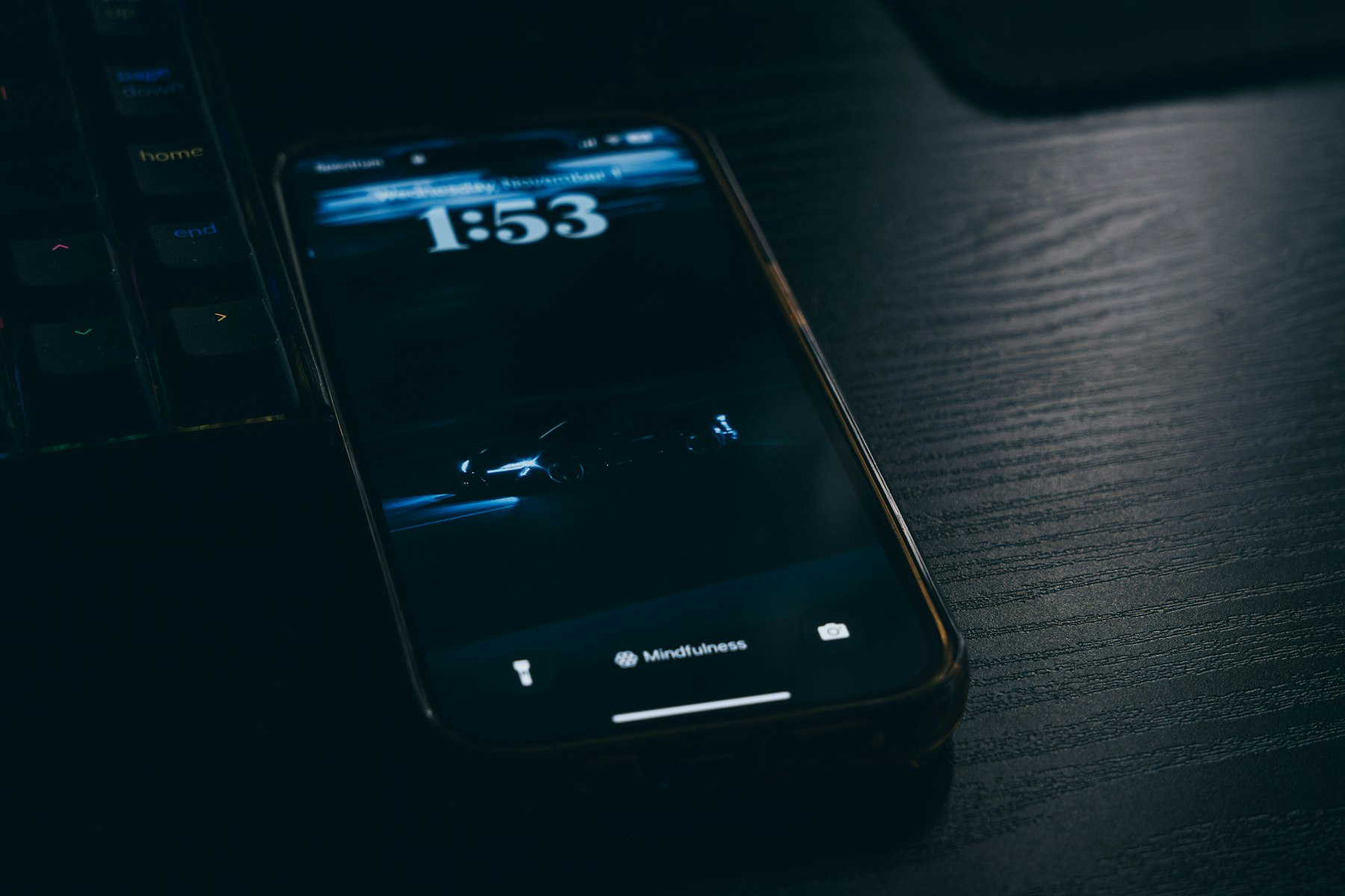 A phone on a dark desk beside a keyboard, its screen showing the time